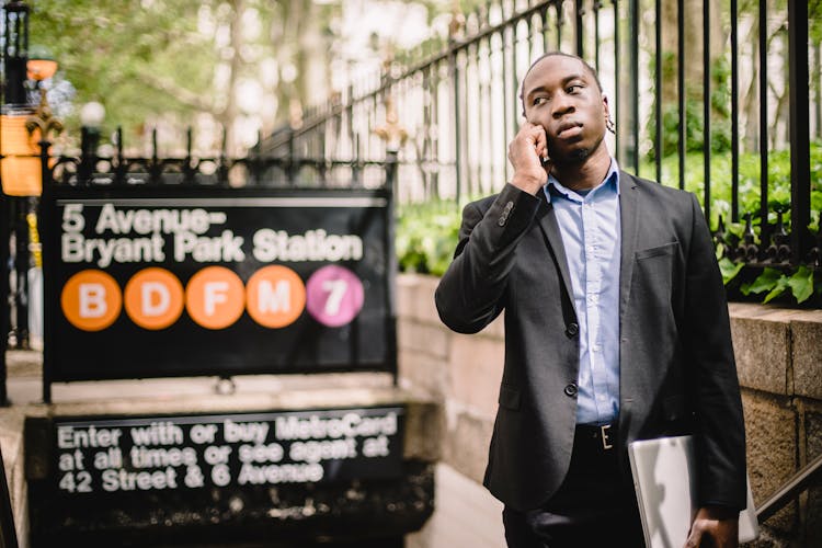 Pensive Black Businessman Talking On Smartphone Near Metro Station Entrance