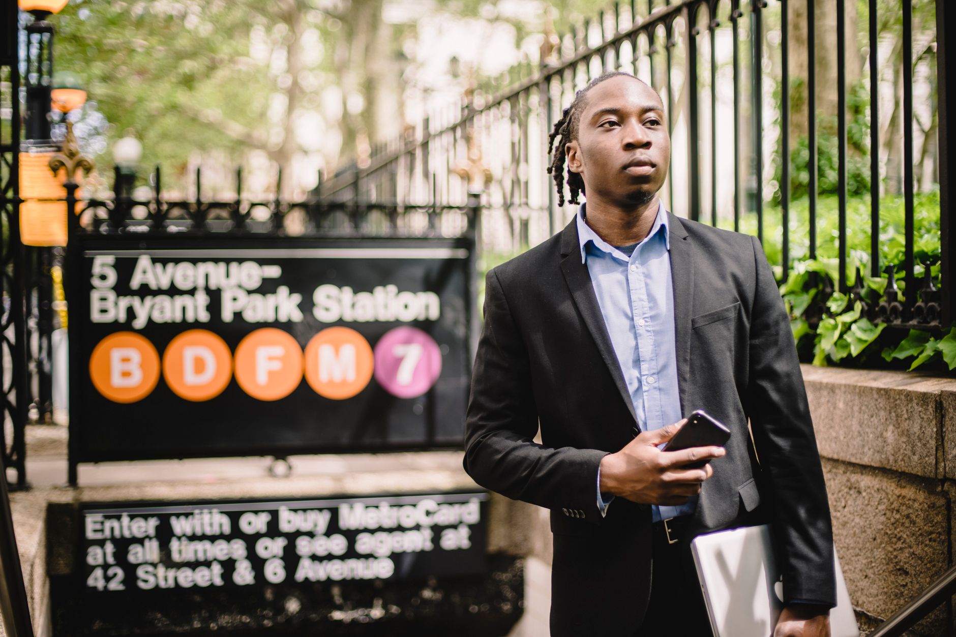 Thoughtful African American businessman wearing classy formal suit standing on stairs near metro station with mobile phone and looking away pensively