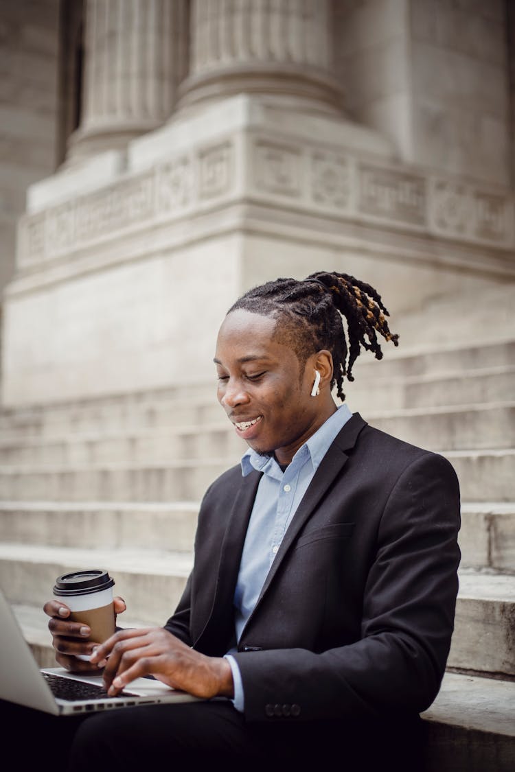 Cheerful Black Businessman Typing On Laptop On Building Stairs