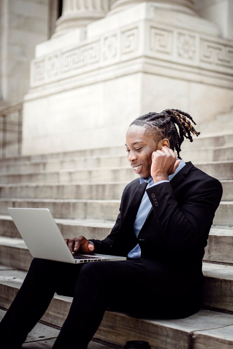 Happy Black Businessman With Earbuds And Laptop On Building Staircase