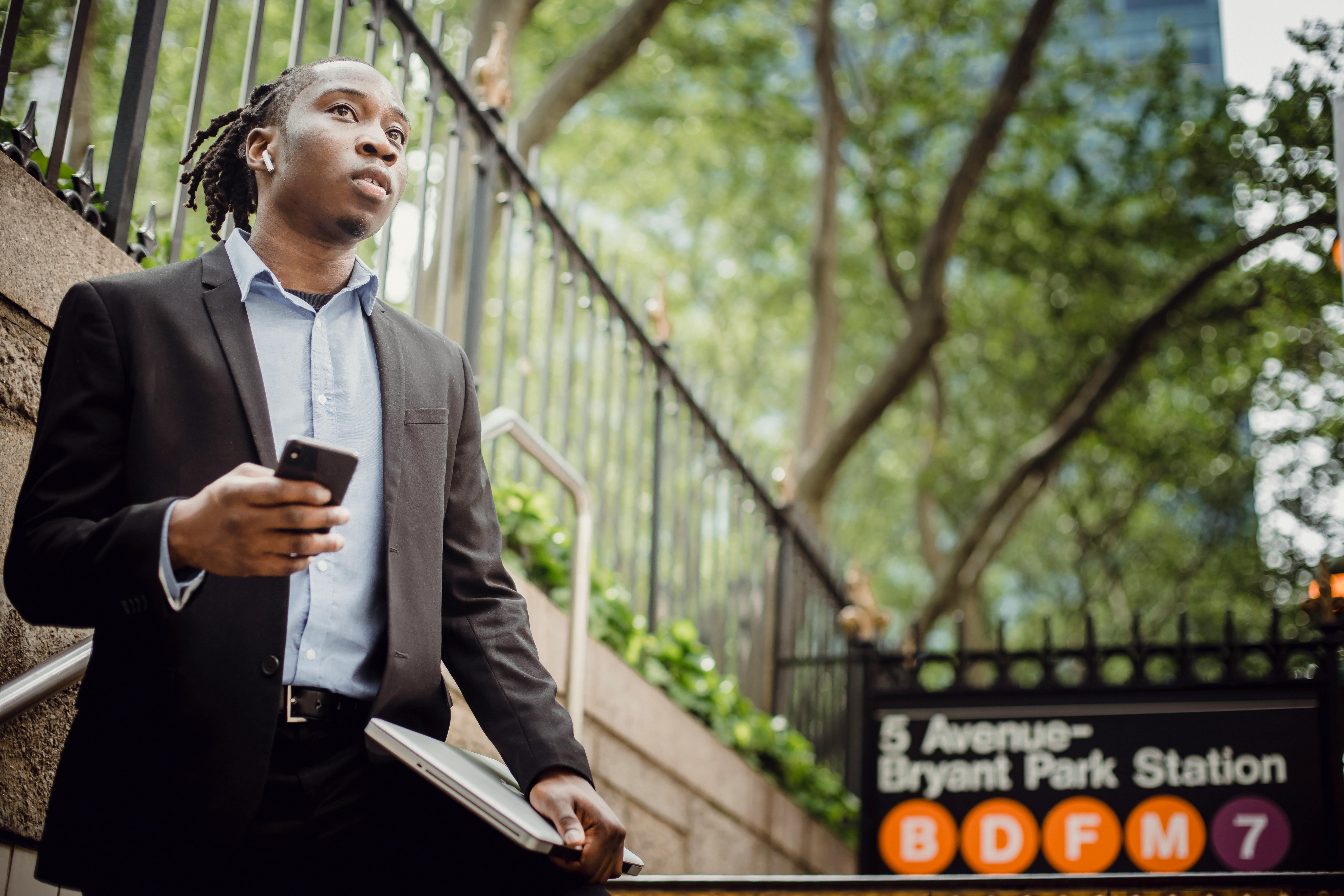 pensive black businessman with earbuds using smartphone on street