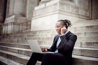 一位穿着西装的自信商人，在户外石阶上使用着笔记本电脑和耳机