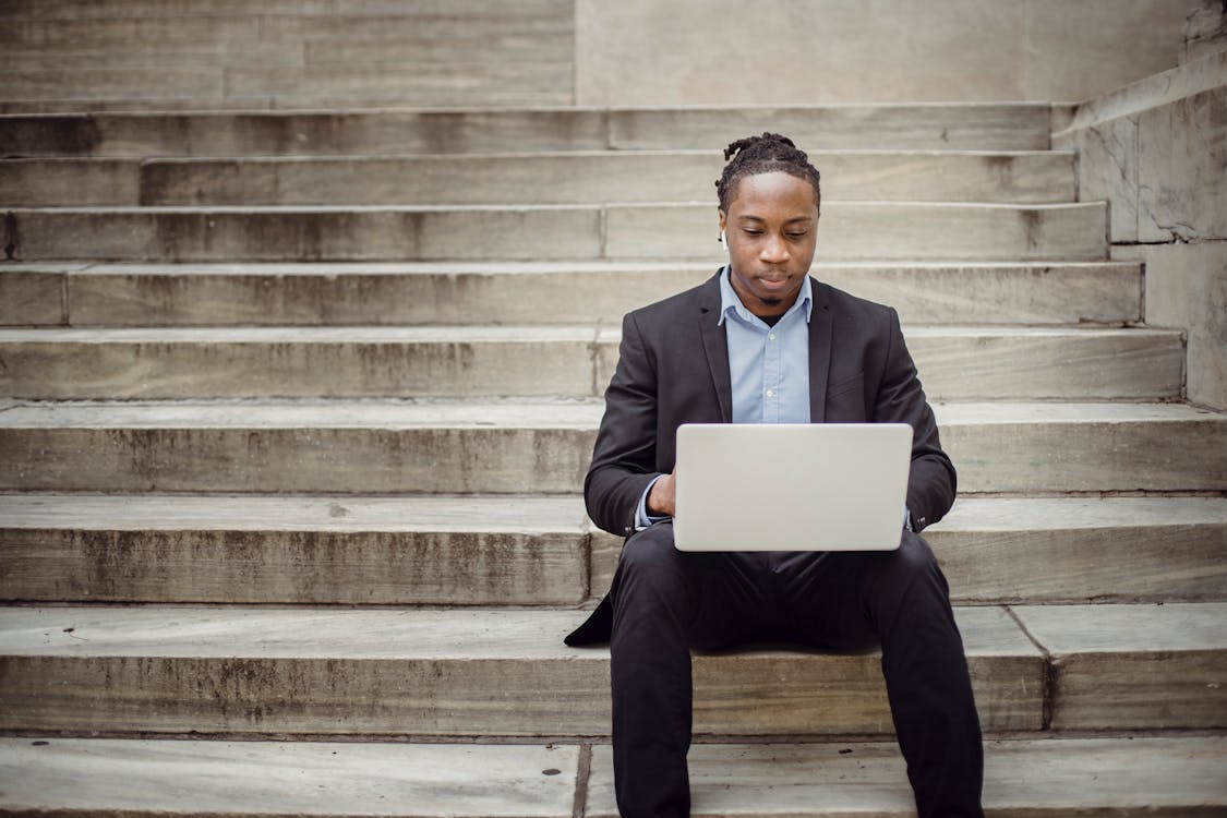 Free Focused black businessman working on laptop remotely on street steps Stock Photo
