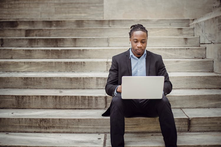 Focused Black Businessman Working On Laptop Remotely On Street Steps