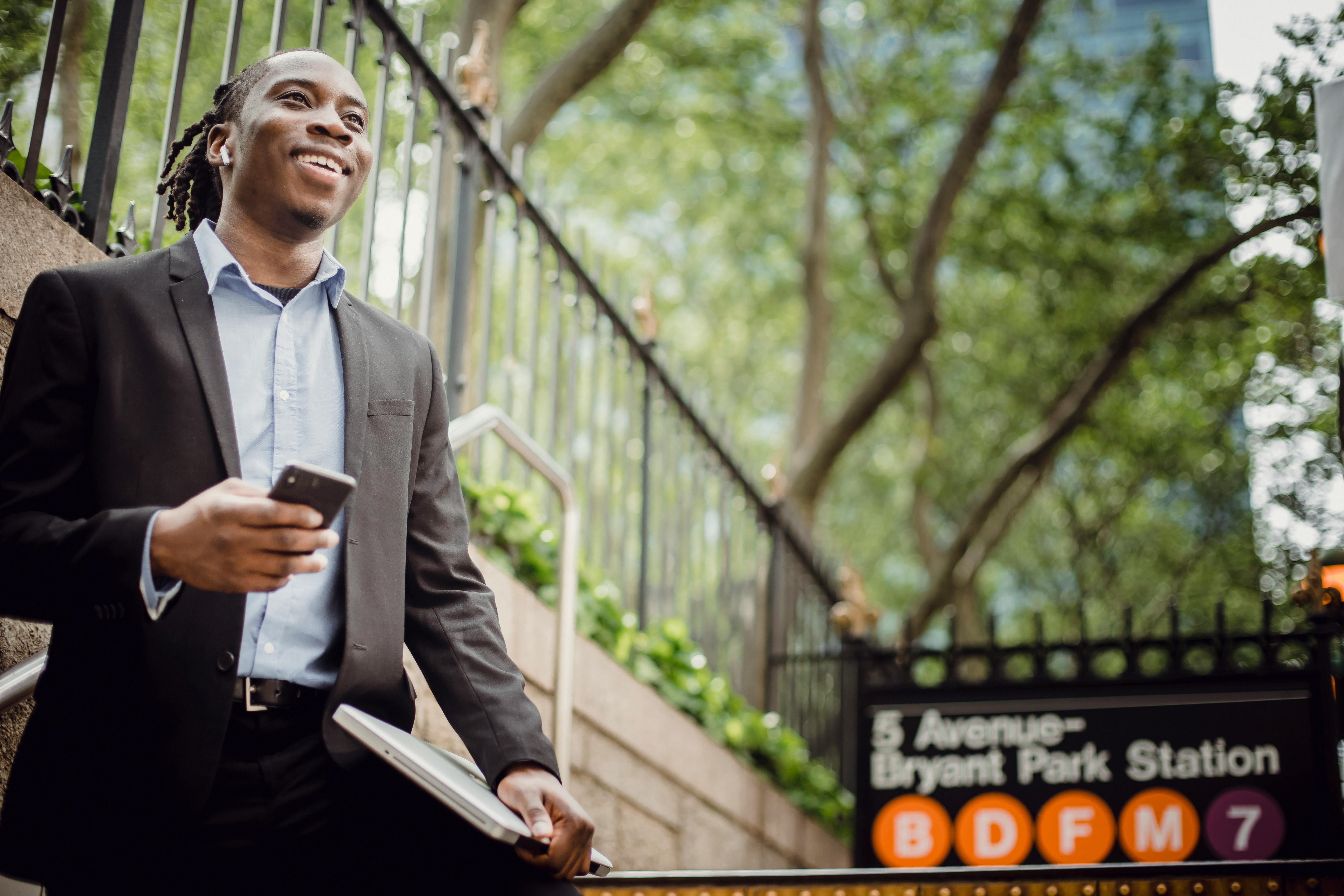 cheerful black businessman with smartphone near metro station