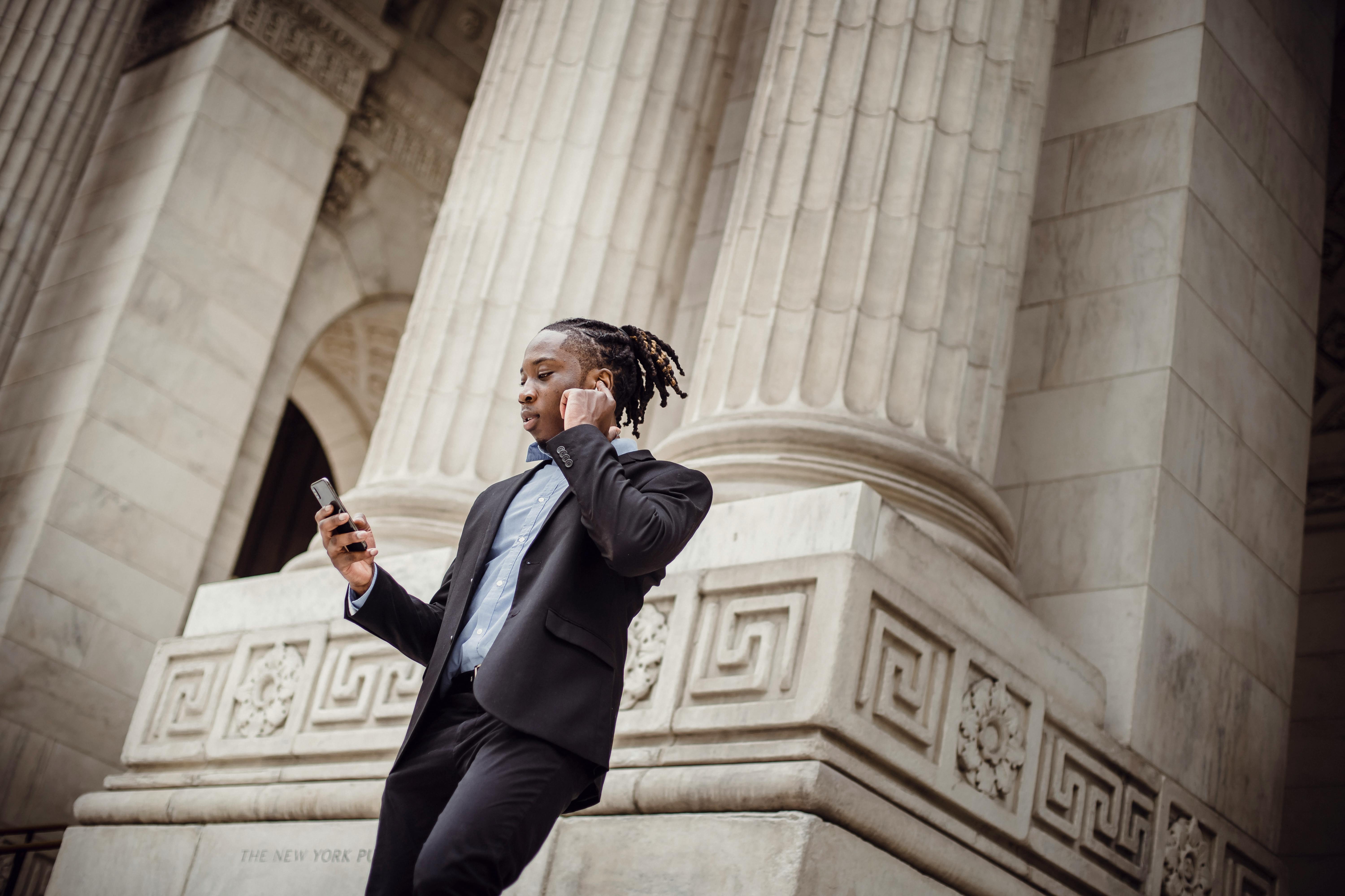 focused african american male employee speaking on smartphone using tws earphones in downtown