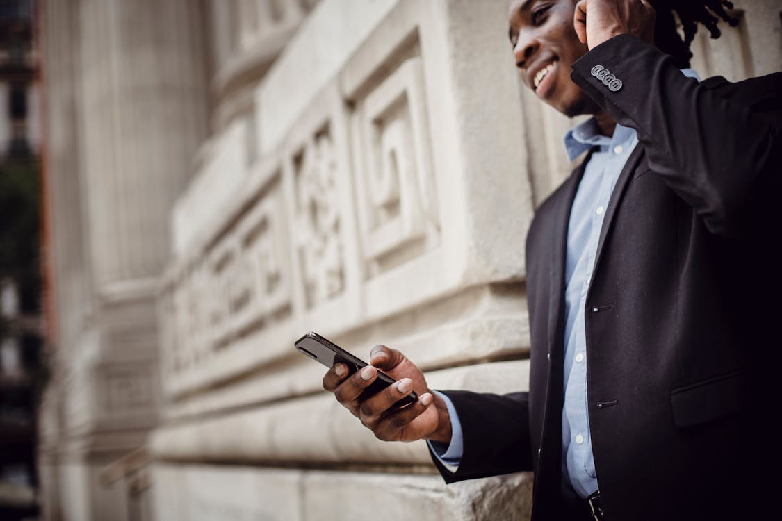 Smiling black male manager communicating on smartphone outside modern building