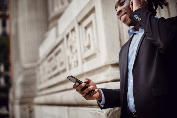 Smiling Black Male Manager Communicating On Smartphone Outside Modern Building