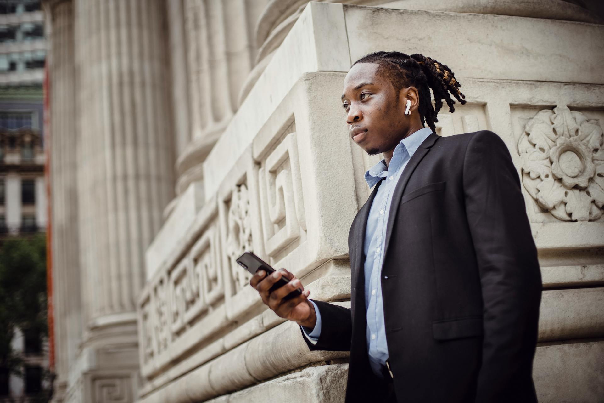 Pensive black businessman waiting on street with smartphone in hand