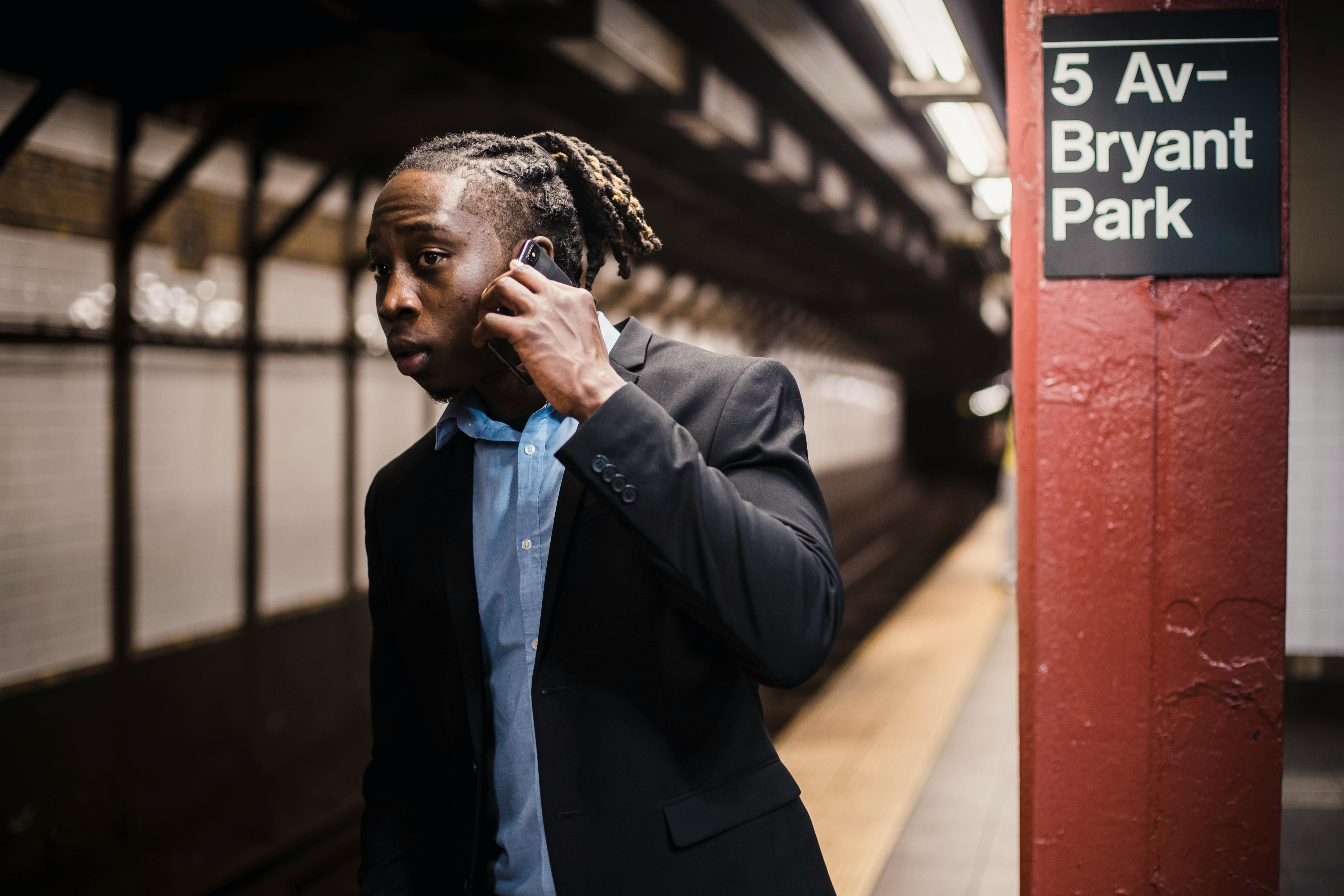 African American male in formal wear talking on mobile phone and looking into subway tunnel with worried expression