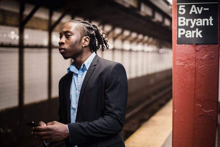 Serious Young Office Worker With Mobile Waiting For Underground Train