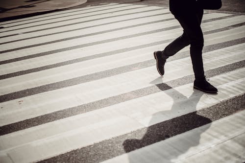 Crop faceless person in elegant black trousers and shoes walking on crosswalk in daytime