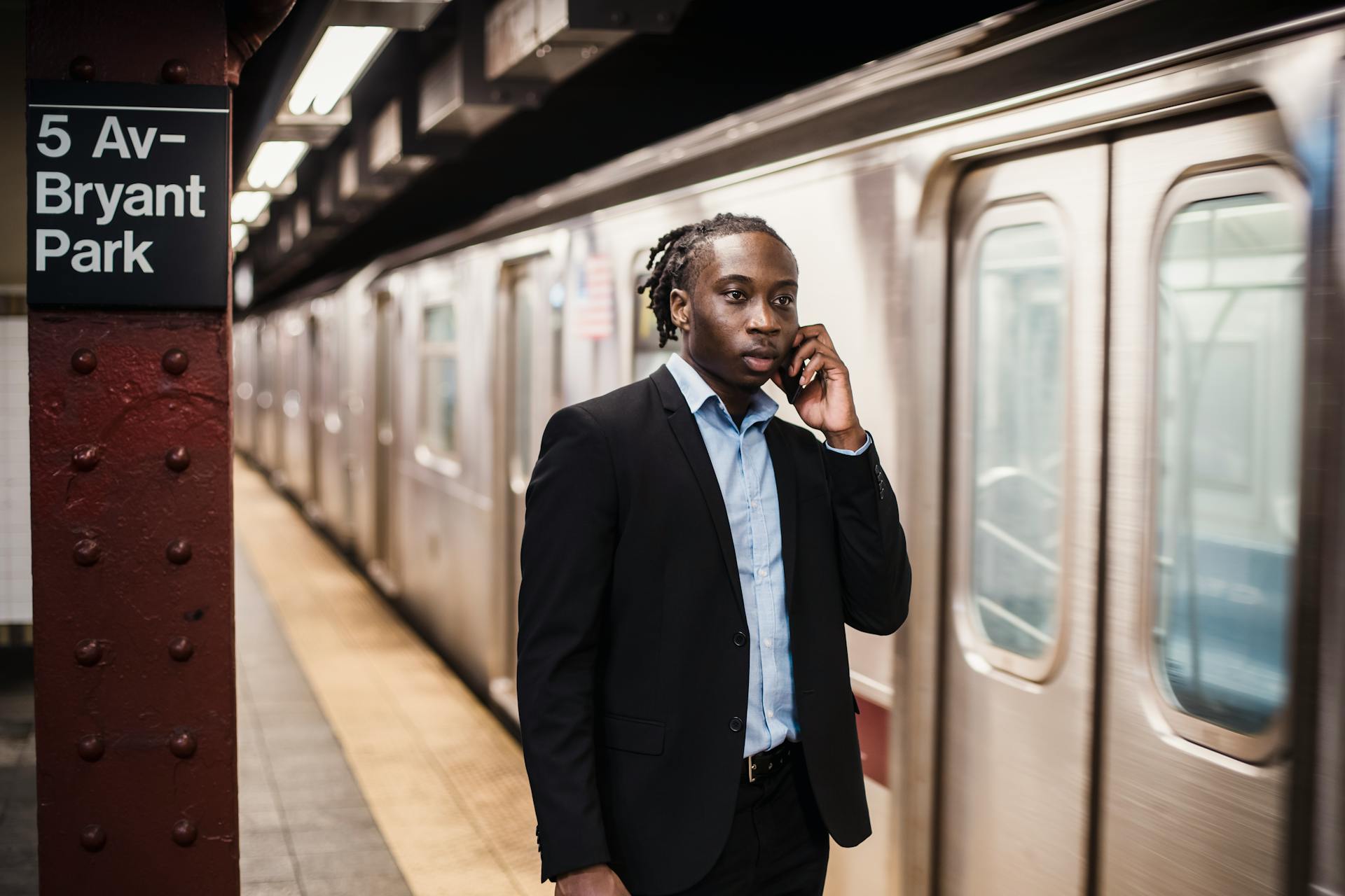 Serious African American male in formal suit talking on smartphone while waiting for underground train to stop