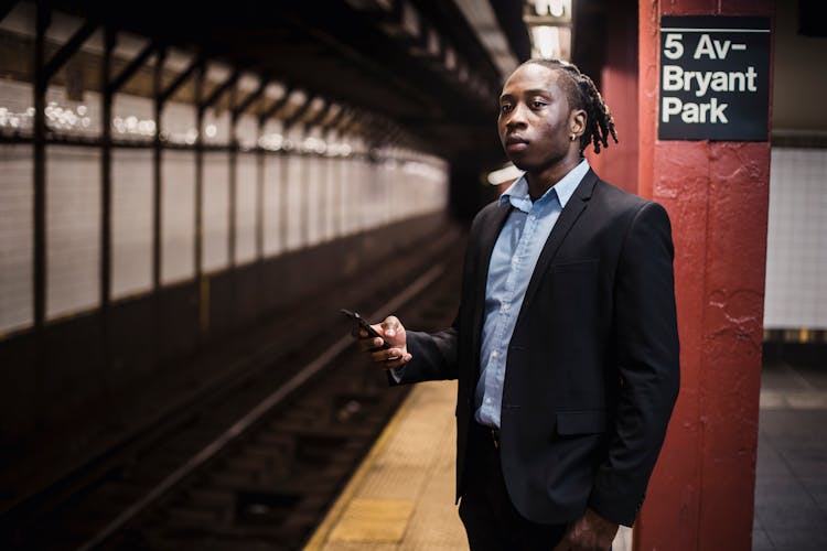 Serious Commuter With Smartphone Waiting For Train At Underground Station