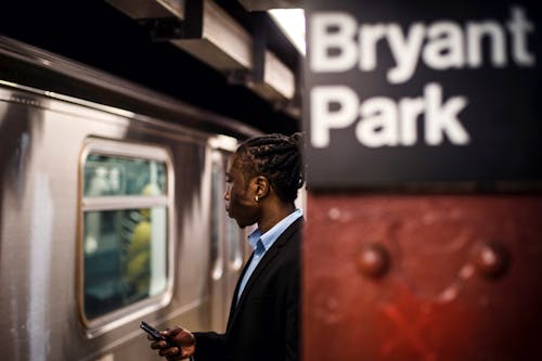 Side view of smart African American male with cellphone in hand waiting for arriving subway train to stop