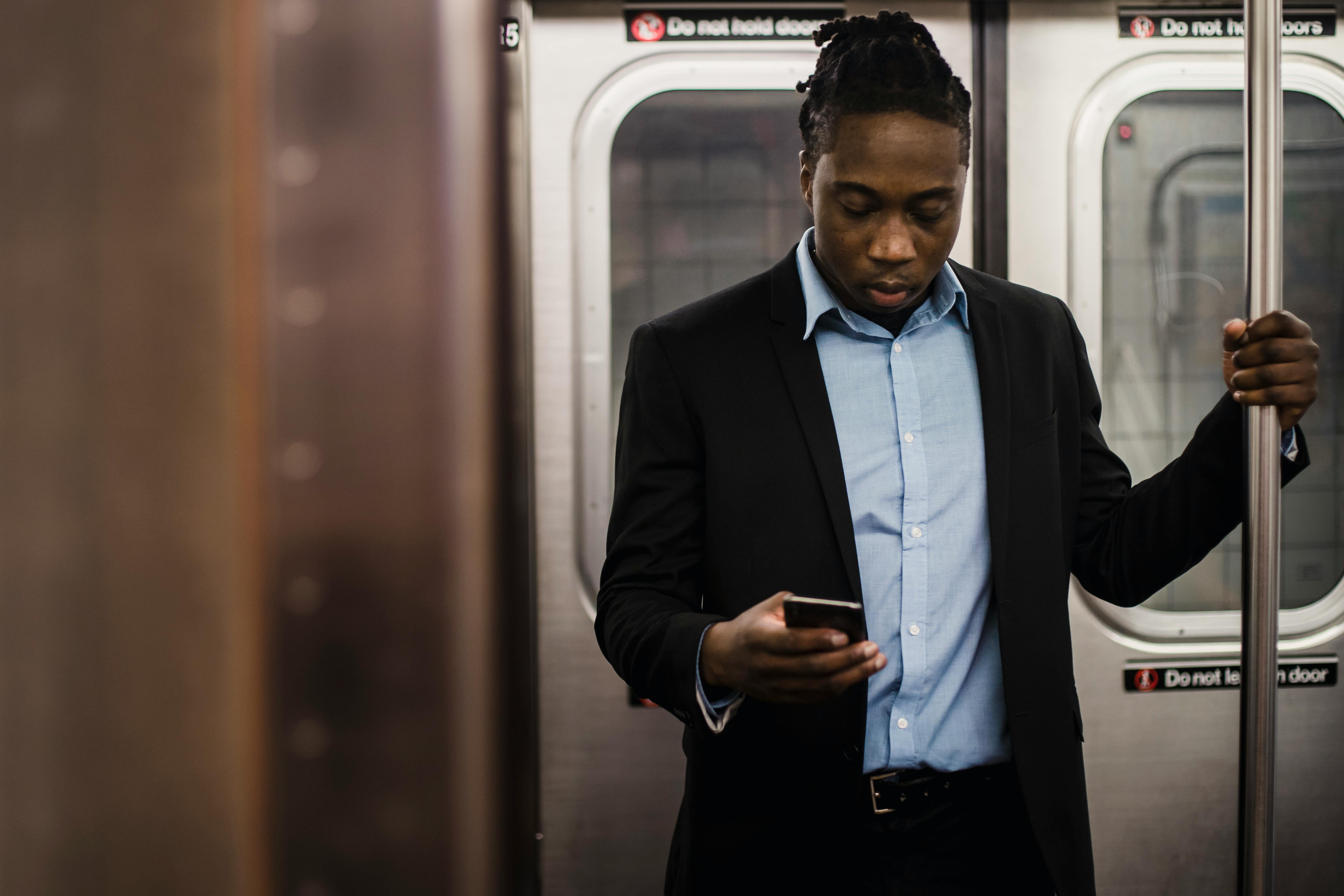 serious black office employee using smartphone on train