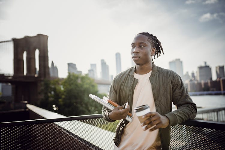 Young Black Man With Cup Of Coffee And Notebooks