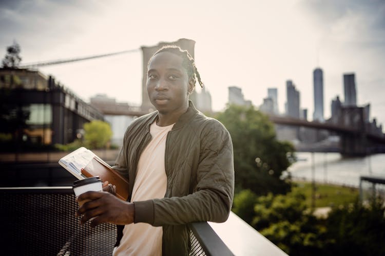 Serious Male Student With Coffee And Books Relaxing On Balcony