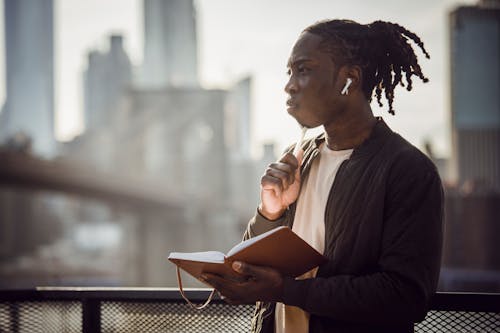 Free Thoughtful black man in wireless earphones with notepad on balcony Stock Photo