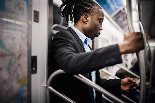 Free Side view of crop wistful African American passenger with pigtails in formal wear using social media on cellphone while commuting to work on subway Stock Photo