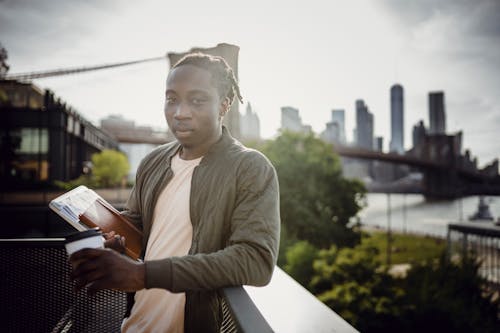 Free Wistful black student standing on balcony with coffee and notebook Stock Photo