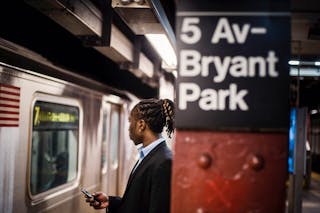 Black worker with smartphone waiting for subway at metro station