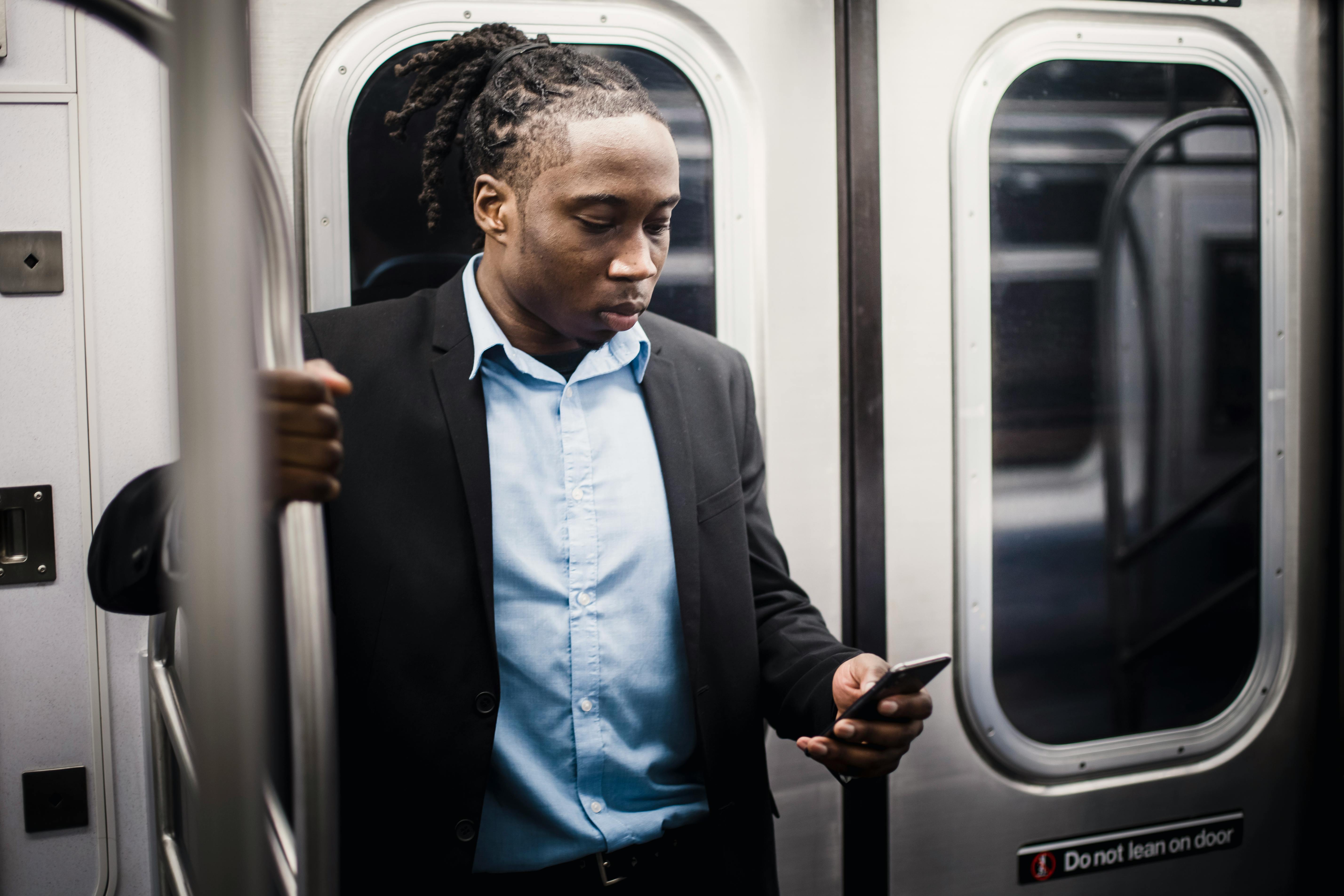 serious black passenger browsing internet on smartphone on subway train