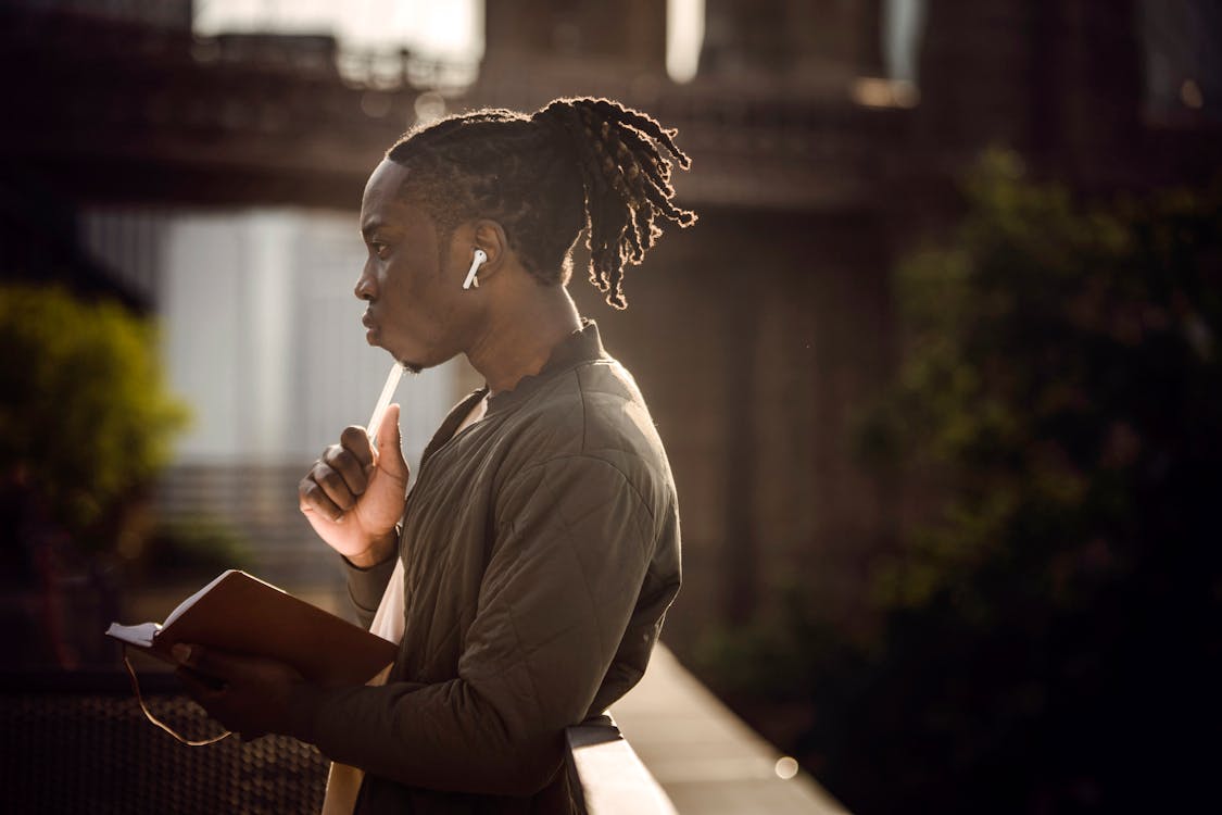 Young thoughtful black male student with notebook in city park