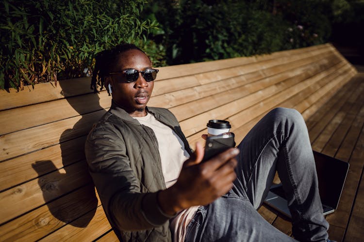 Young Black Man Taking Selfie On Bench In Park