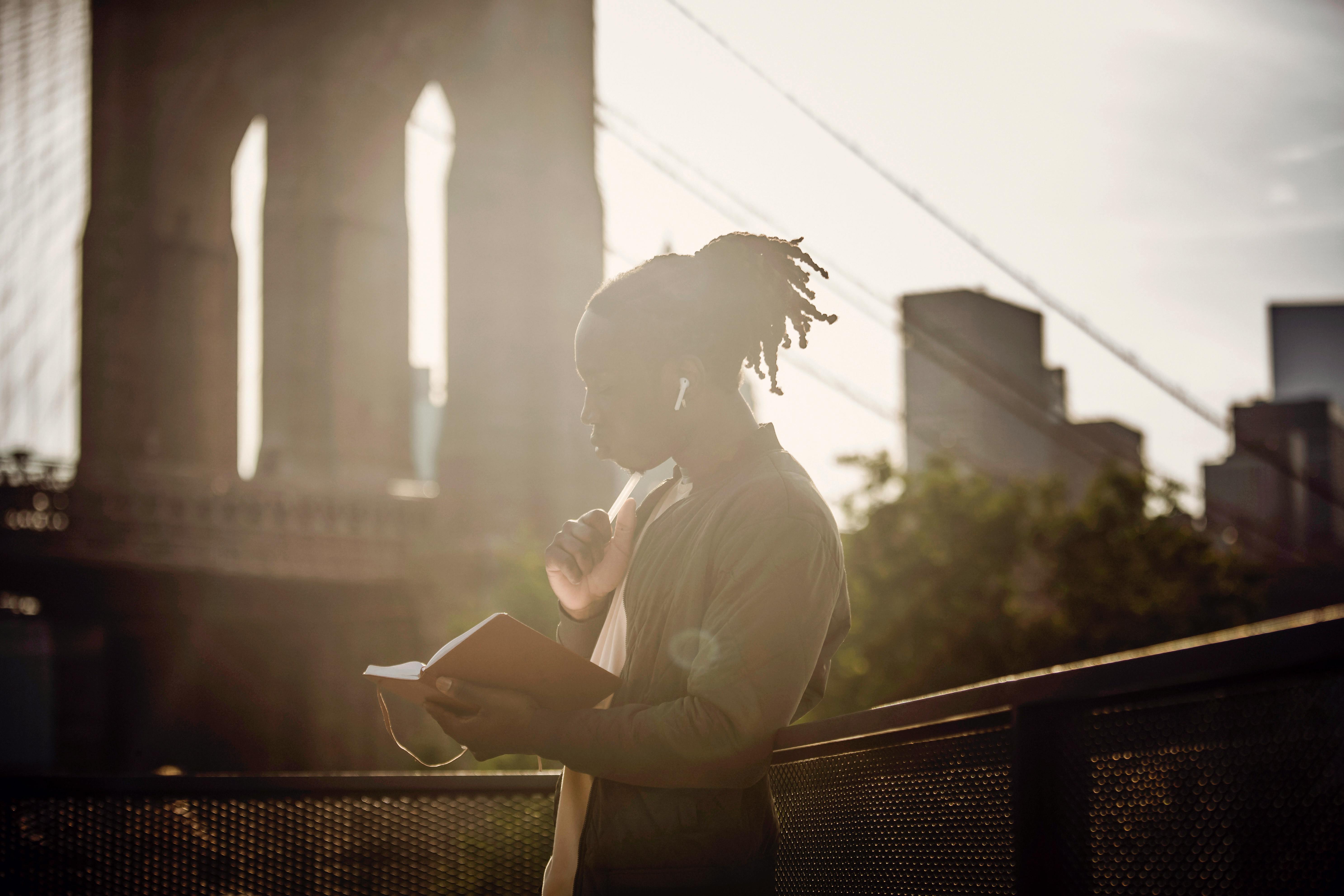 thoughtful young african american guy reading notebook on city embankment on sunny day