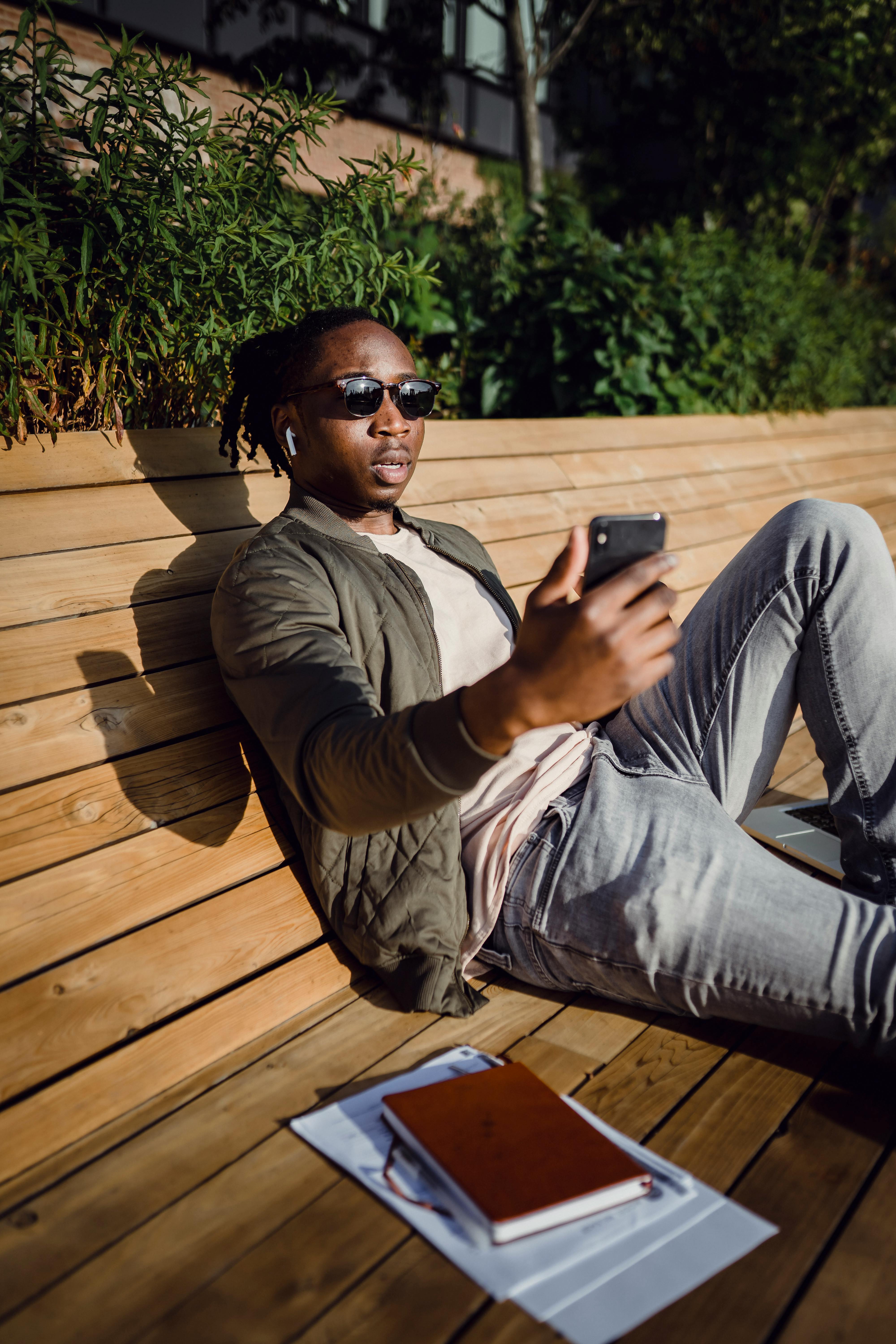 young black guy chatting on smartphone sitting on wooden bench
