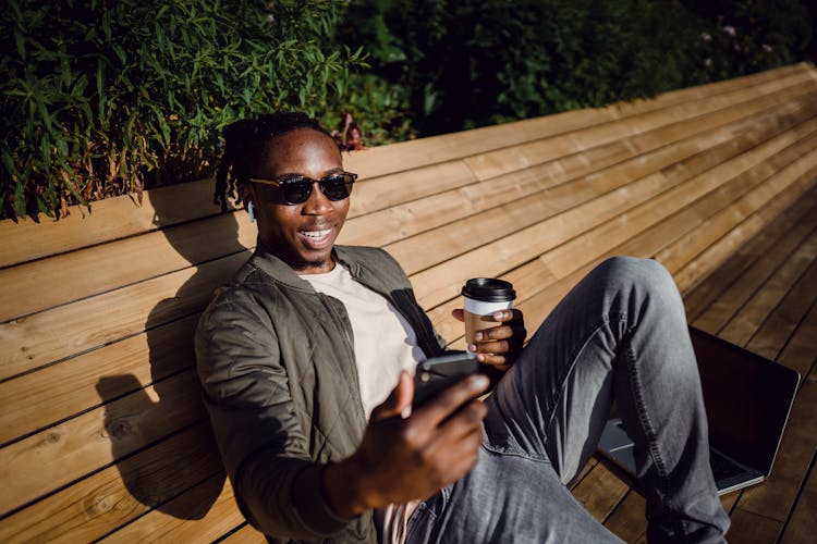 Cheerful Young Black Man Having Video Conversation Via Smartphone During Coffee Break In Park