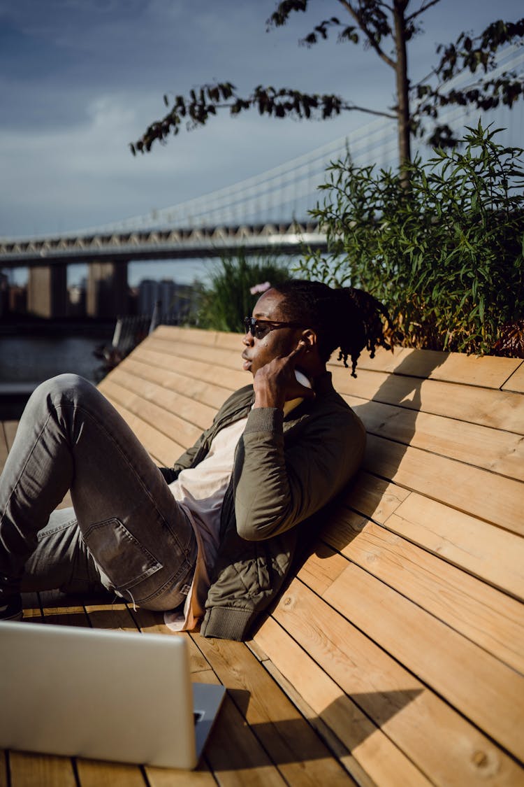 Confident Black Man Relaxing On Wooden Bench In Park With Netbook