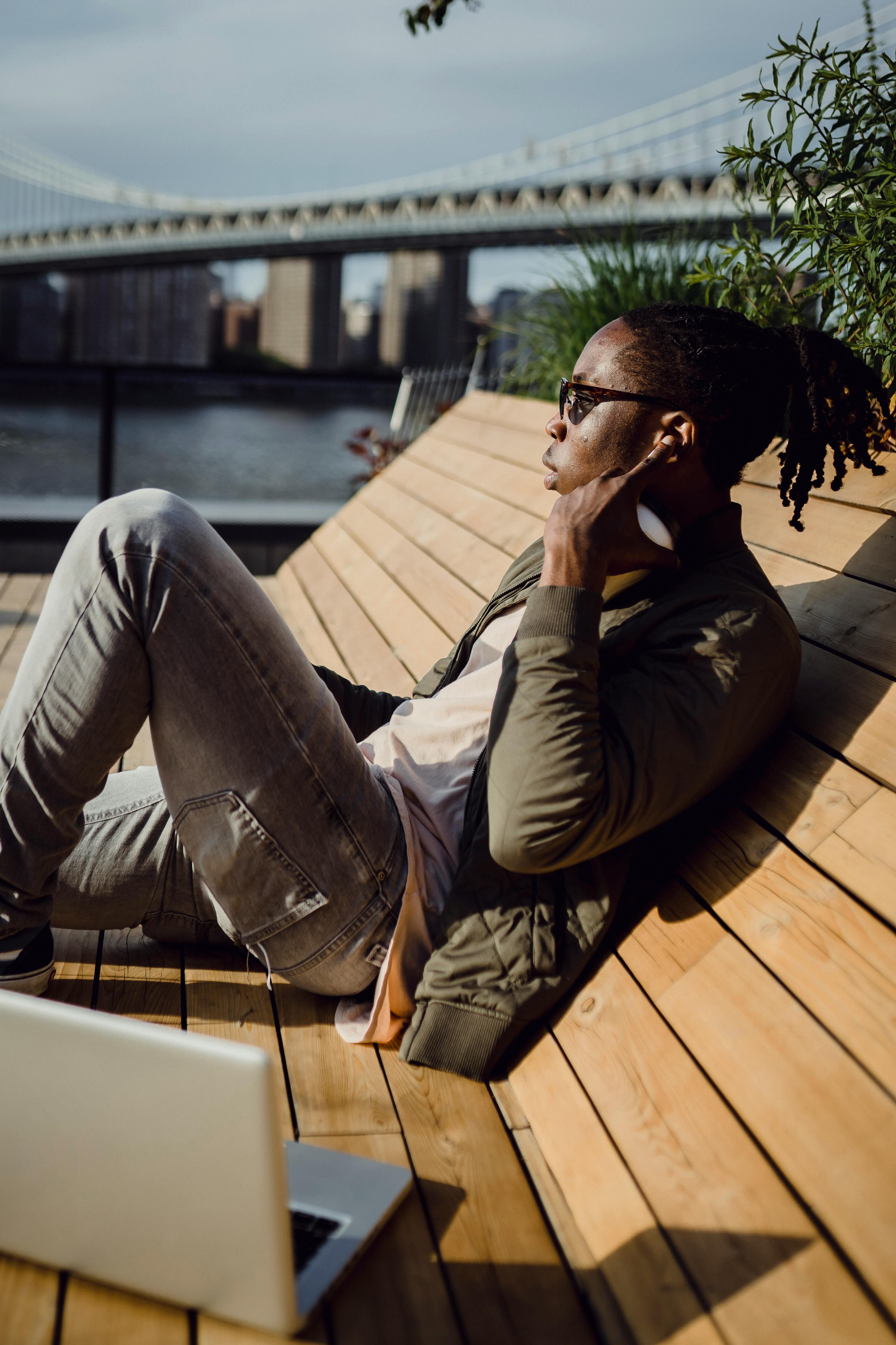 african american guy spending weekend on bench in park with laptop