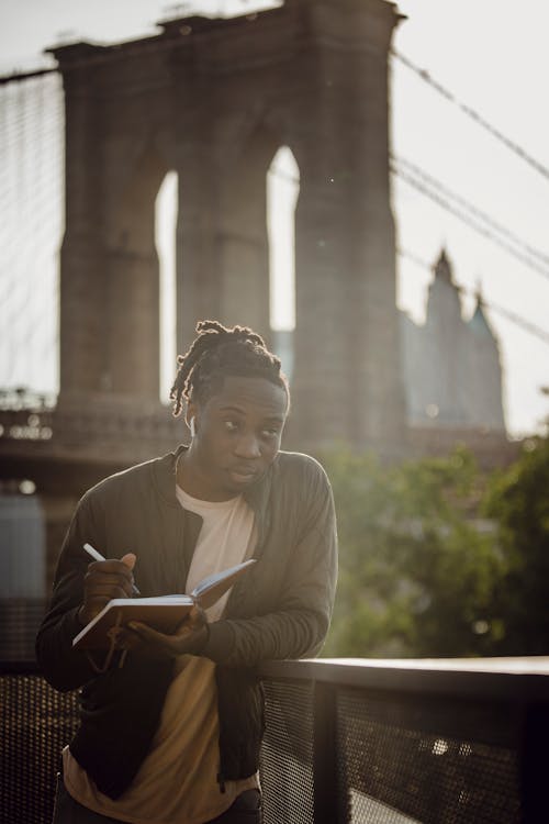 Free Positive black male freelancer writing ideas while standing on city embankment Stock Photo