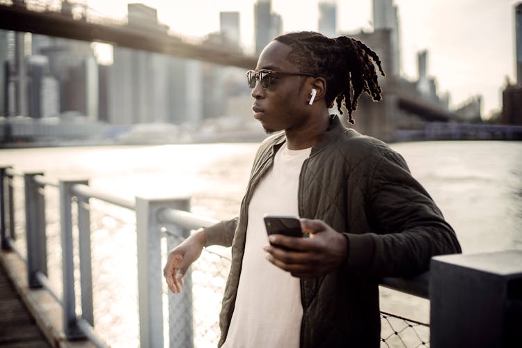 Black Man In Wireless Earphones Listening To Music From Smartphone