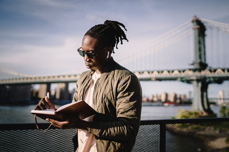 African American Man In Wireless Earphones With Organizer On Bridge