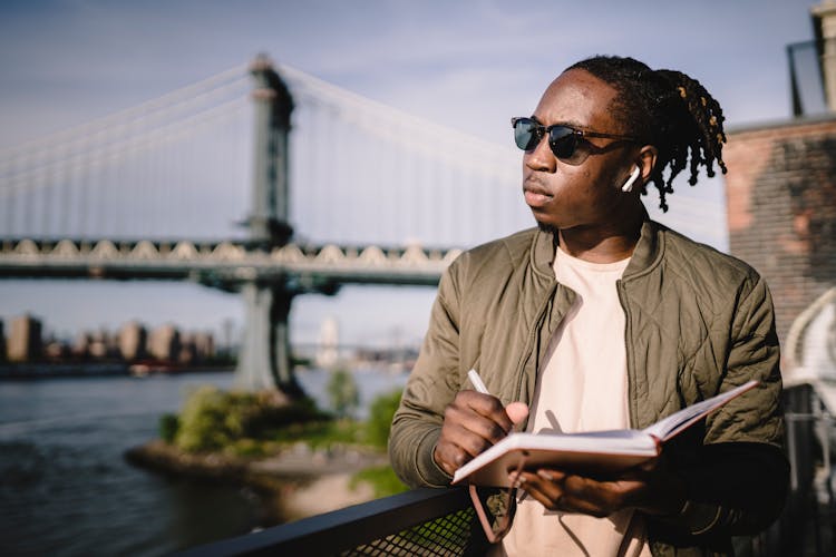 Contemplative Black Man In Wireless Earphones Writing In Notebook