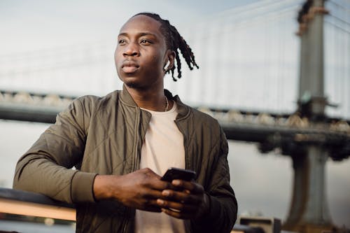 Free Low angle of young serious African American looking away while surfing smartphone and listening to music in earphones Stock Photo