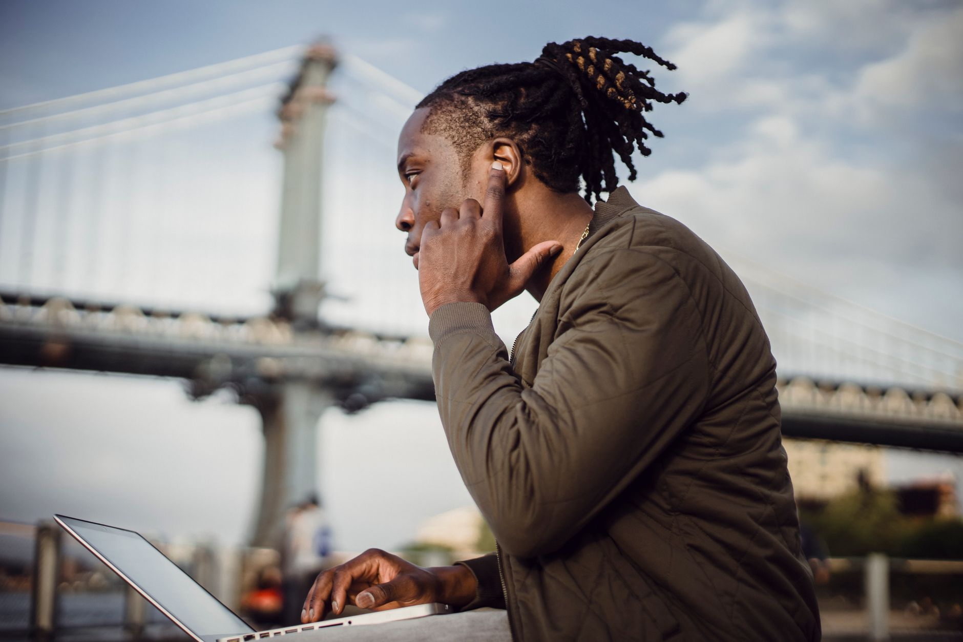 Focused businessman using a laptop in a city setting with a bridge background.