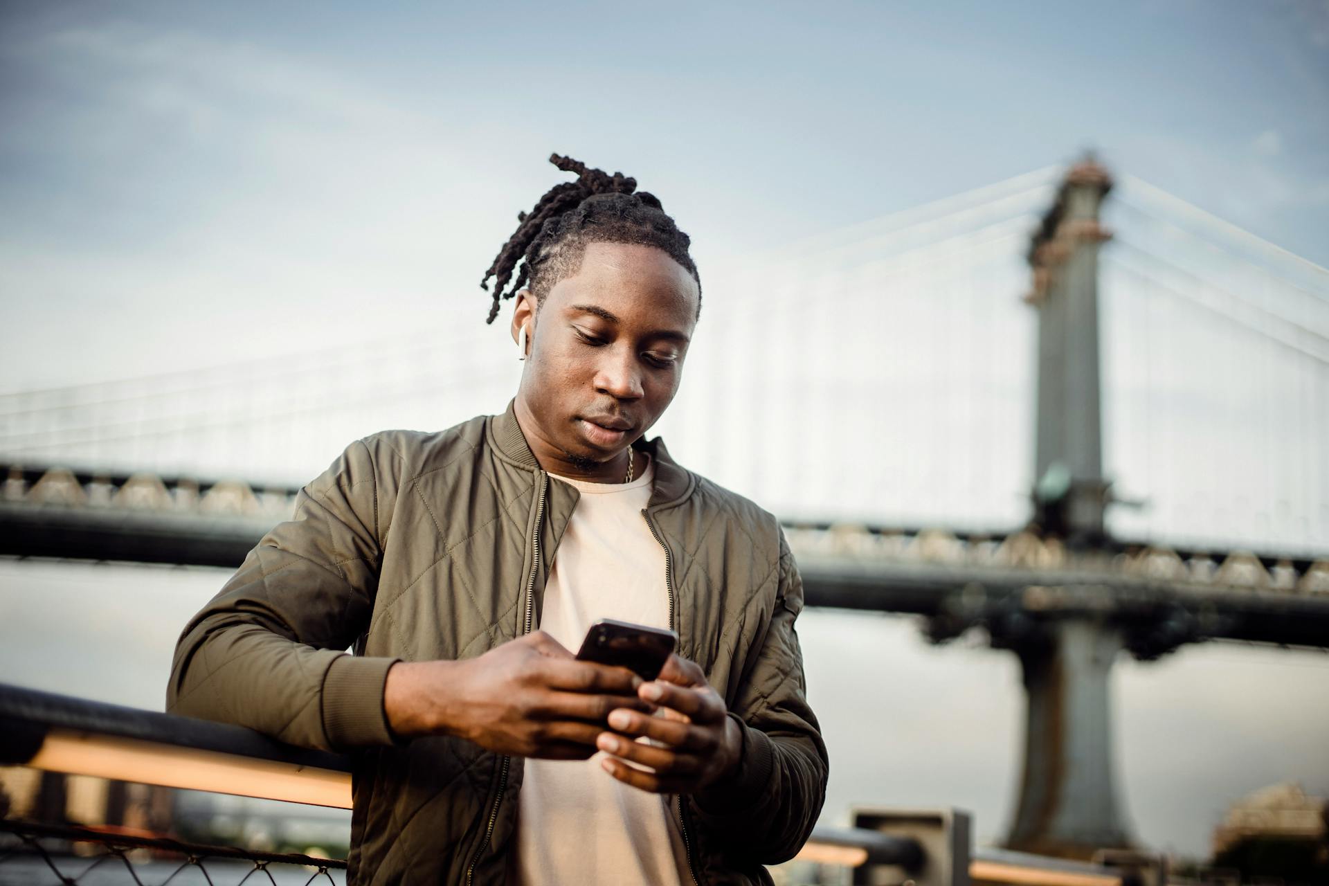 From below of serious black man in earphones scrolling smartphone while listening to music outside and looking down