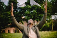 Happy African American remote worker tossing papers in air happy to get rid of boring paperwork while sitting in green park