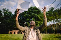 Black man in casual clothes throwing sheets of paper up while working in city park in sunny day
