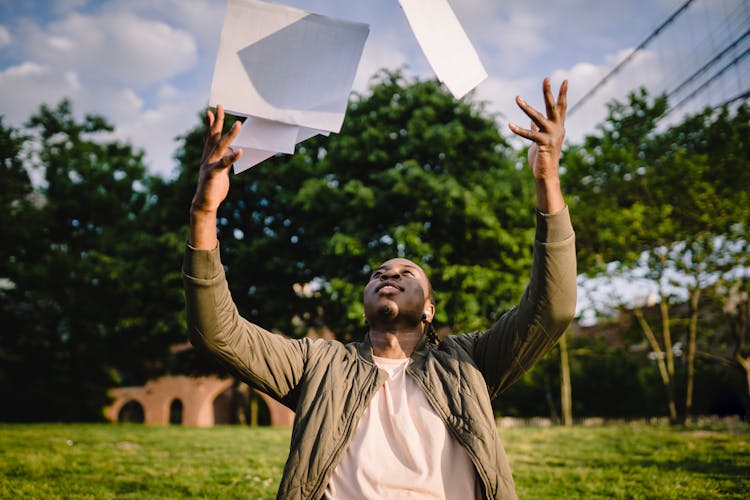 African American Man Throwing Paper Sheets Up In Park