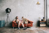 在时尚的工业环境中，一个留着胡子的男人和一只狗坐在皮沙发上微笑