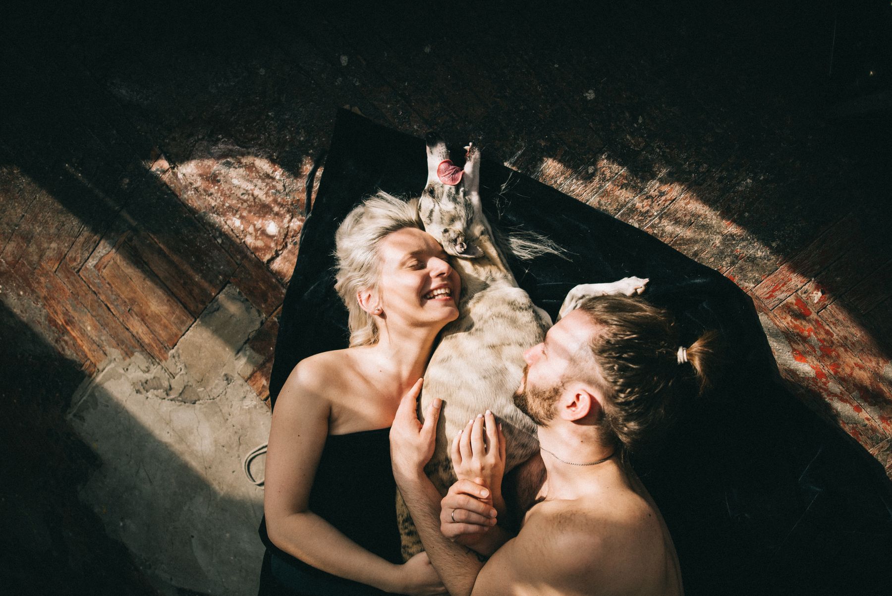 Happy couple cuddling their dog on the floor at home