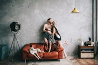 一对夫妇在室内拿着吉他，和一只放松的狗一起在红色沙发上拥抱