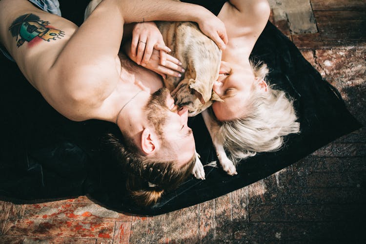 A Couple With Their Pet Dog Lying On Black Textile