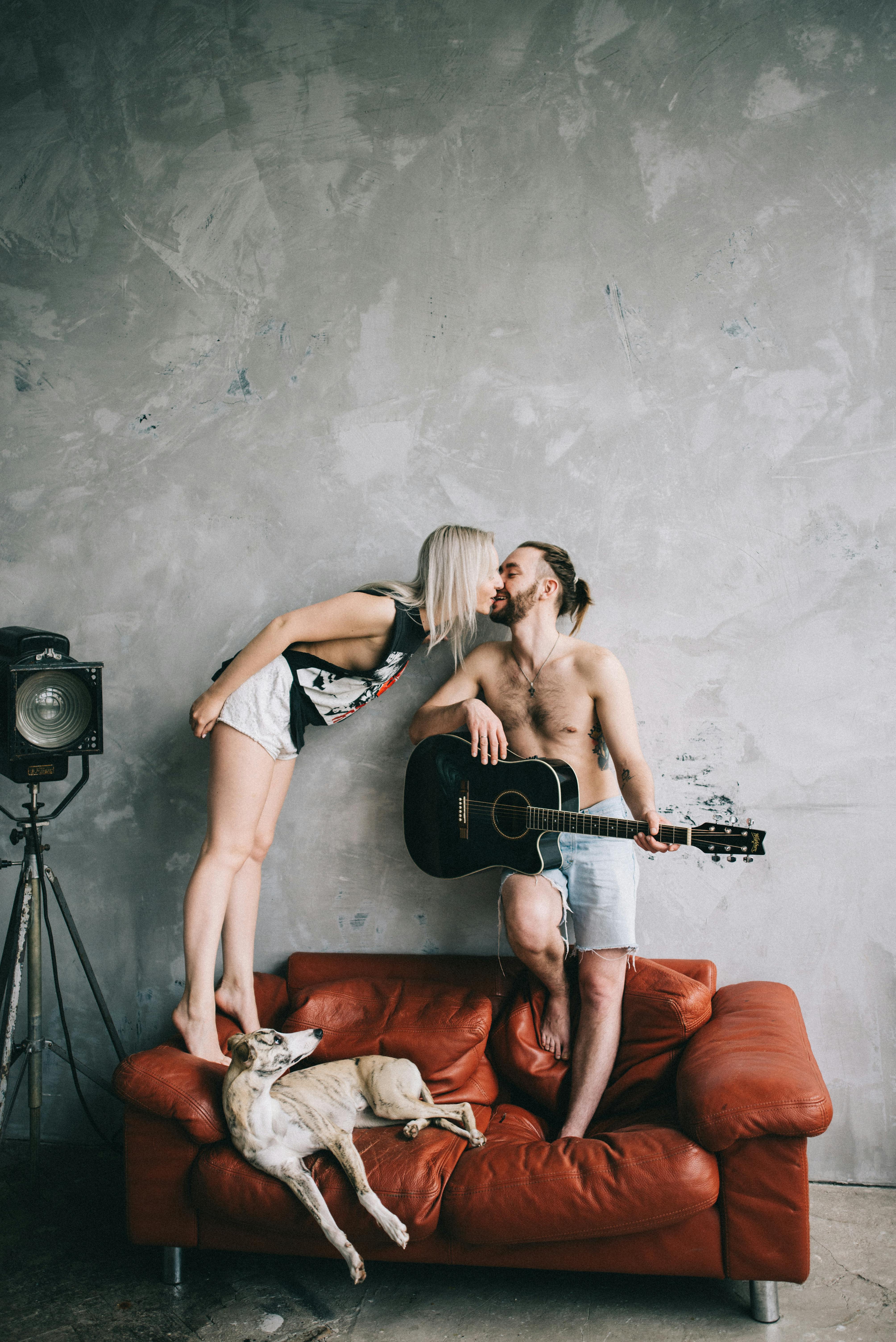 一对快乐的夫妇在红色沙发上与他们的狗接吻，用一把老式吉他伴奏