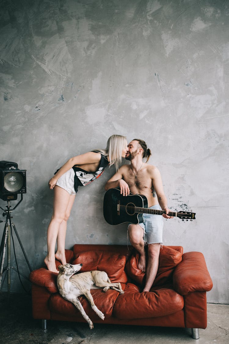 A Couple Kissing While Standing On A Couch 